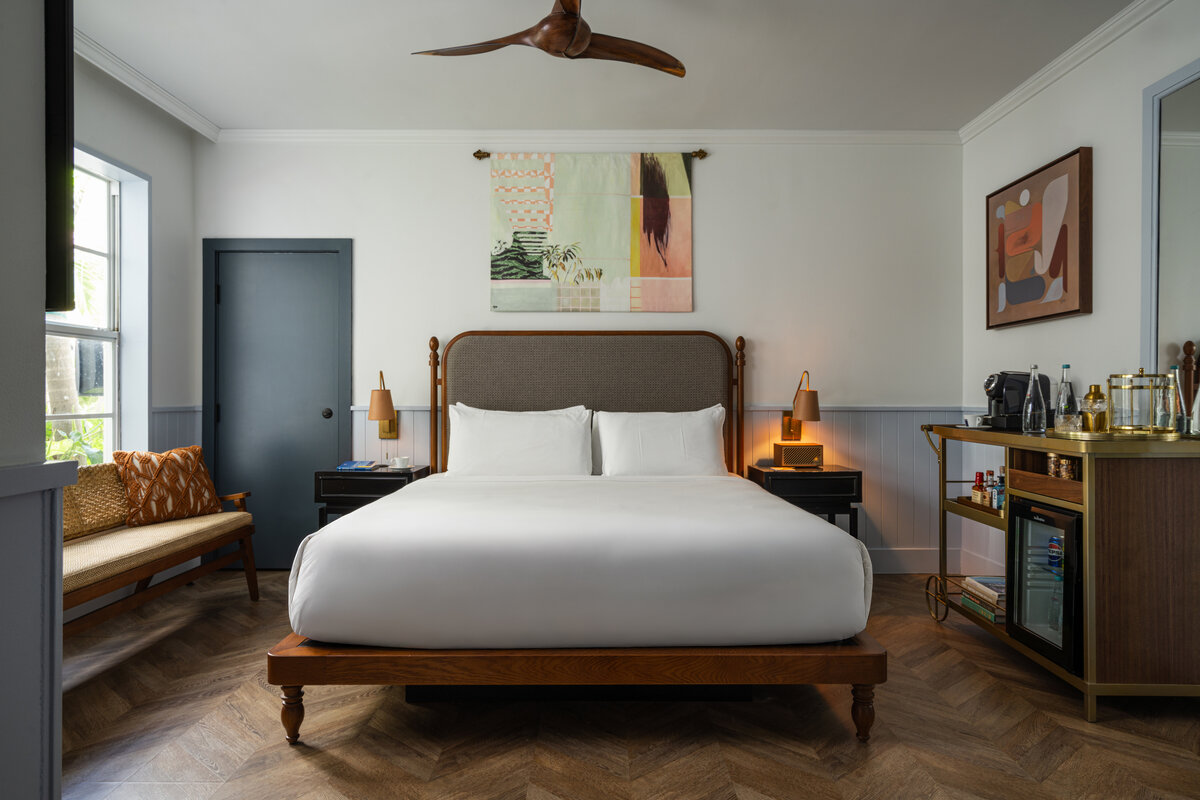 A wide view of a hotel room with a king-sized bed, nightstands, a mini-fridge, and artwork on the walls.